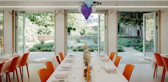 A room with white walls opening out into a garden, with long tables and balloons for a party