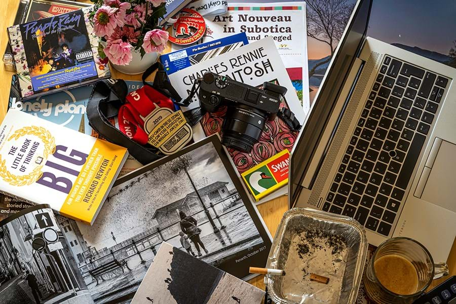 Books, an ashtray, box of matches and a laptop on a table 