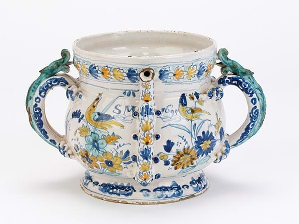 A white cup with three handles, decorated with blue and yellow flowers