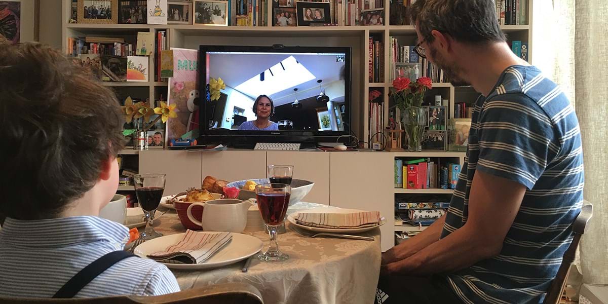 Child and adult eating Easter lunch looking at a screen showing a video call
